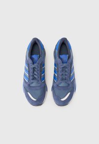 Blue athletic sneakers with a mix of mesh and suede materials, featuring three white stripes, textured panels, and a rounded toe design.
