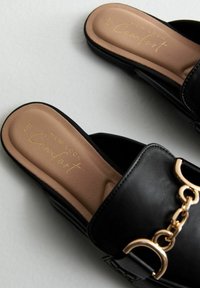 Černé nazouvací sandály s hladkým povrchem, zdobené zlatým řetízkem na pásku a polstrovanou béžovou stélkou s vyraženým logem.