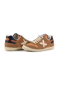 Sneakers in suede marrone con suola testurizzata crema, lacci bianchi e dettagli blu navy. Presentano un design cucito e una toppa con il logo sulla linguetta.