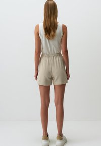 Beige, elastische taille shorts van zachte stof, met een relaxte pasvorm. Gemaakt met een wit mouwloos topje en witte sneakers.