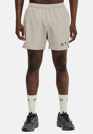 Shorts de sport gris clair avec une taille élastique, poches latérales et logo "ATW" noir sur la cuisse gauche ; associés à des baskets noires et des chaussettes blanches.