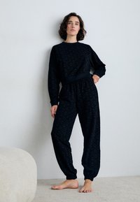 Il completo loungewear nero presenta un motivo testurizzato. La parte superiore ha maniche lunghe e una vita elastica. I pantaloni hanno polsini elasticizzati e una vestibilità comoda.