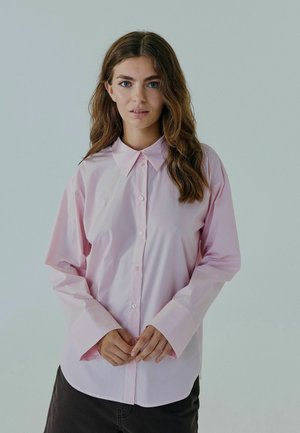 Lyserød langærmet skjorte med knaplukning, klassisk krave og opkrøllede ærmer, der har en glat tekstur og minimalt design.