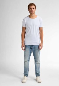 Hvid kortærmet T-shirt med rund halsudskæring, kombineret med lyseblå denimjeans og hvide sneakers; står på en neutral baggrund.