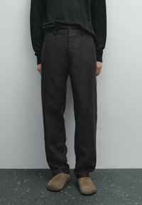 Tummanruskeat, väljät housut, joissa on sileä pinta, normaali vyötärönauha, etutaskut ja suora lahjemalli.