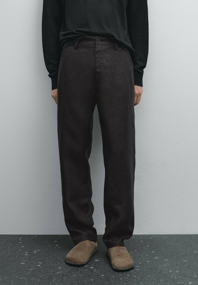 Tummanruskeat, väljät housut, joissa on sileä pinta, normaali vyötärönauha, etutaskut ja suora lahjemalli.