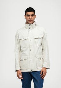 Chaqueta beige con un alto cuello, dos bolsillos en el pecho y cierres a presión. Fabricada con una tela suave y un acabado ligeramente texturizado.