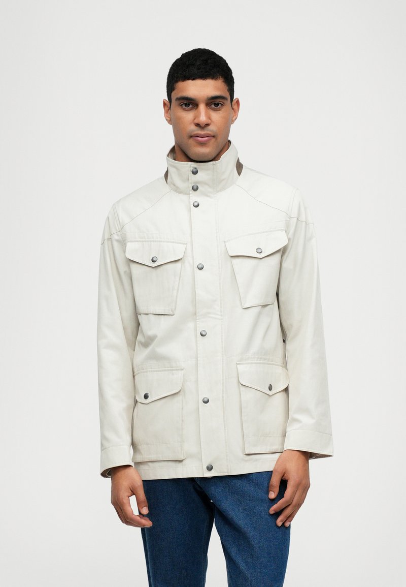 Chaqueta beige con un alto cuello, dos bolsillos en el pecho y cierres a presión. Fabricada con una tela suave y un acabado ligeramente texturizado.