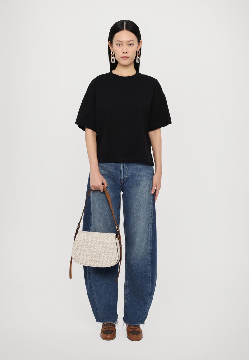 T-shirt noir oversize, jean baggy bleu taille haute, et sac bandoulière crème avec un motif géométrique et une sangle brune. Chaussures à plateforme marron.