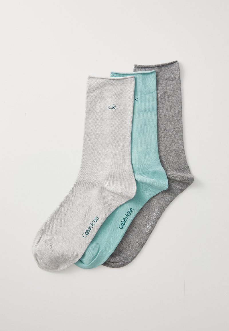 Tres pares de calcetines Calvin Klein doblados en gris claro, verde menta y gris oscuro, dispuestos superpuestos sobre un fondo blanco.