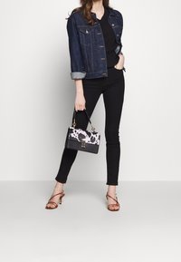Borsa nera con una patta a pois neri e rosa, accessori dorati, indossata con una giacca di jeans, top nero e jeans skinny neri. Tacchi con cinturini marroni.