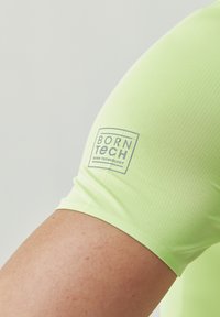 Maglietta sportiva a maniche corte di un vivace verde lime, realizzata in tessuto leggero. Presenta un piccolo logo grigio sulla spalla sinistra.