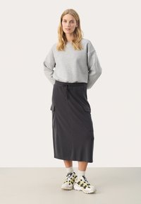 Grijze oversized sweatshirt gecombineerd met een zwarte midi-rok met zijkanten en een trekkoord in de taille. Draagt het met geprinte sneakers en sokken.