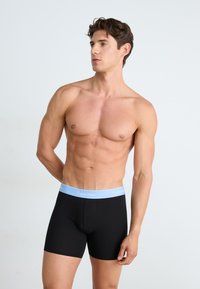 Zwarte boxershorts met een lichtblauwe Calvin Klein tailleband. Gladde stofstructuur, aansluitend ontwerp en lengte tot halverwege de dij.