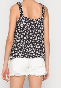 Black floral tank top with white daisies, ruffled straps, and a loose fit, paired with frayed white denim shorts.