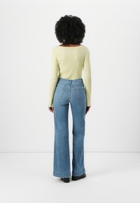 Top a maniche lunghe di un verde chiaro a costine abbinato a jeans a gamba larga di un blu chiaro a vita alta. Il tessuto è liscio, con cuciture a contrasto sui polsini.