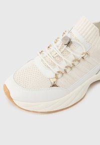 Αθλητικό παπούτσι σε λευκό χρώμα με πλεκτό επάνω μέρος, ελαστικά κορδόνια, χρυσαφένιες λεπτομέρειες και υφασμένο μεσαίο πέλμα· διαθέτει μαξιλαρωμένη φτέρνα και λαστιχένια σόλα.