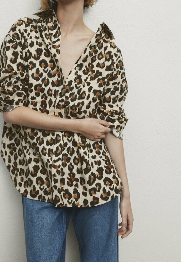 Chemise à boutons imprimé léopard en beige et marron, avec manches longues retroussées aux poignets. Associée à un jean denim bleu clair.