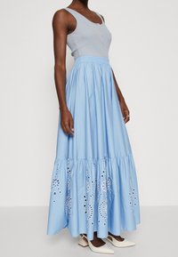 Ljusblå bomullsmaxi kjol med ett lagerdesign, prydd med broderade blommönster och ögla-utskärningar vid fållen. Elastisk midja.