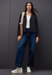 Black cropped jacket with buttons, white v-neck top, dark blue wide-leg jeans, and white high-top sneakers. Brown shoulder bag with fur accents.