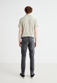 Polo grigio chiaro a maniche corte, abbinato a jeans grigio scuro. I jeans hanno tasche posteriori e sono aderenti, indossati con sneakers nere.