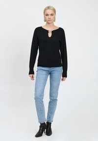 Schwarzer Strickpullover mit einem Keyhole-Ausschnitt, kombiniert mit hellblauen Jeans und schwarzen Stiefeletten. Sanfte Textur und taillierte Passform.