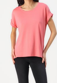 Korallfärgad kortärmad t-shirt med rund halsringning, avslappnad passform och uppvikt ärm. Det mjuka tyget och den lätta draperingen ökar komforten.