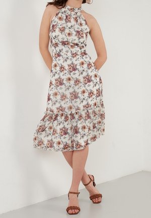 Bloemenjurk met halternek in wit met roze, oranje en groene patronen. Heeft een gerimpelde zoom en is gemaakt van lichtgewicht stof.