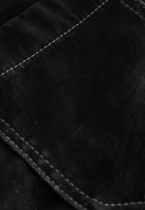 Schwarzer Stoff mit einer glatten Textur, der mit weißen Nähten um eine Tasche verziert ist. Das Gesamterscheinungsbild ist minimalistisch und elegant.