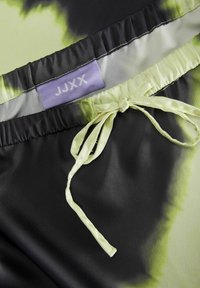 Zwart en groene tie-dye stof met een satijnen textuur. Inclusief een lavendel label en een bijpassende satijnen strik in de taille.