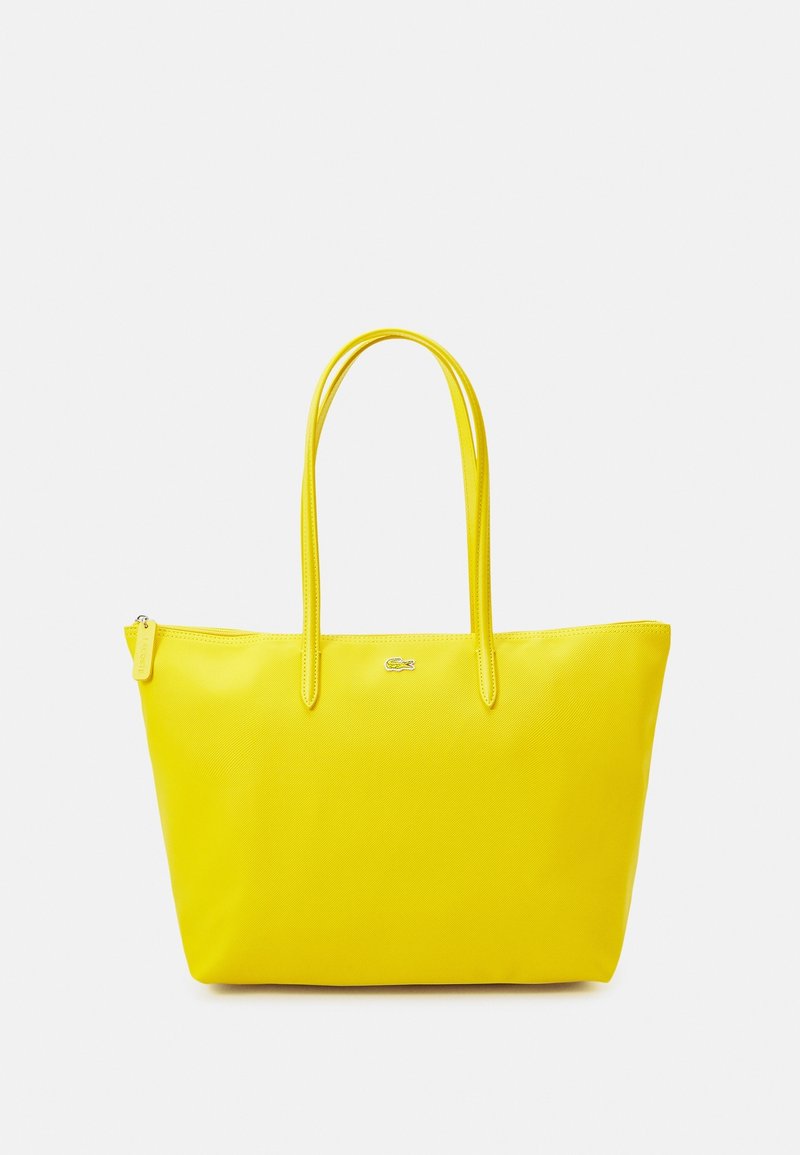 Sac fourre-tout jaune à texture lisse, avec fermeture éclair et deux longues poignées. Comprend un petit logo sur le devant. Design léger.