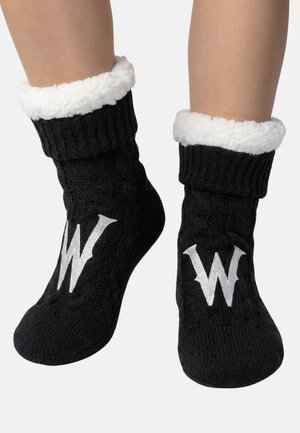 Zwarte gebreide warme sokken met witte fleeceboorden en grote witte "W" letters bovenop, gedragen aan de voeten tegen een neutrale achtergrond.