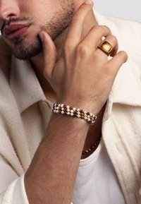 Close-up of a man wearing a white shirt, showing a beaded bracelet with white and amber beads and a gold ring with a large amber stone.