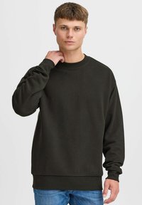 Mørkegrønn hettegenser i avslappet passform, med ribbestrikkede mansjetter og kant, rund hals og myk tekstur. Modellen bruker den med blå jeans.