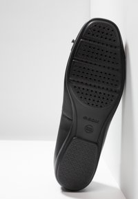 Semelle de chaussure en cuir noir avec perforations, caoutchouc texturé pour l'adhérence et branding subtil. Bords lisses et forme arrondie.