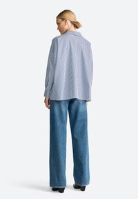 Blue and white striped oversized shirt, lightweight fabric, long sleeves, curved hem, paired with loose-fitting blue denim jeans and block heels.
