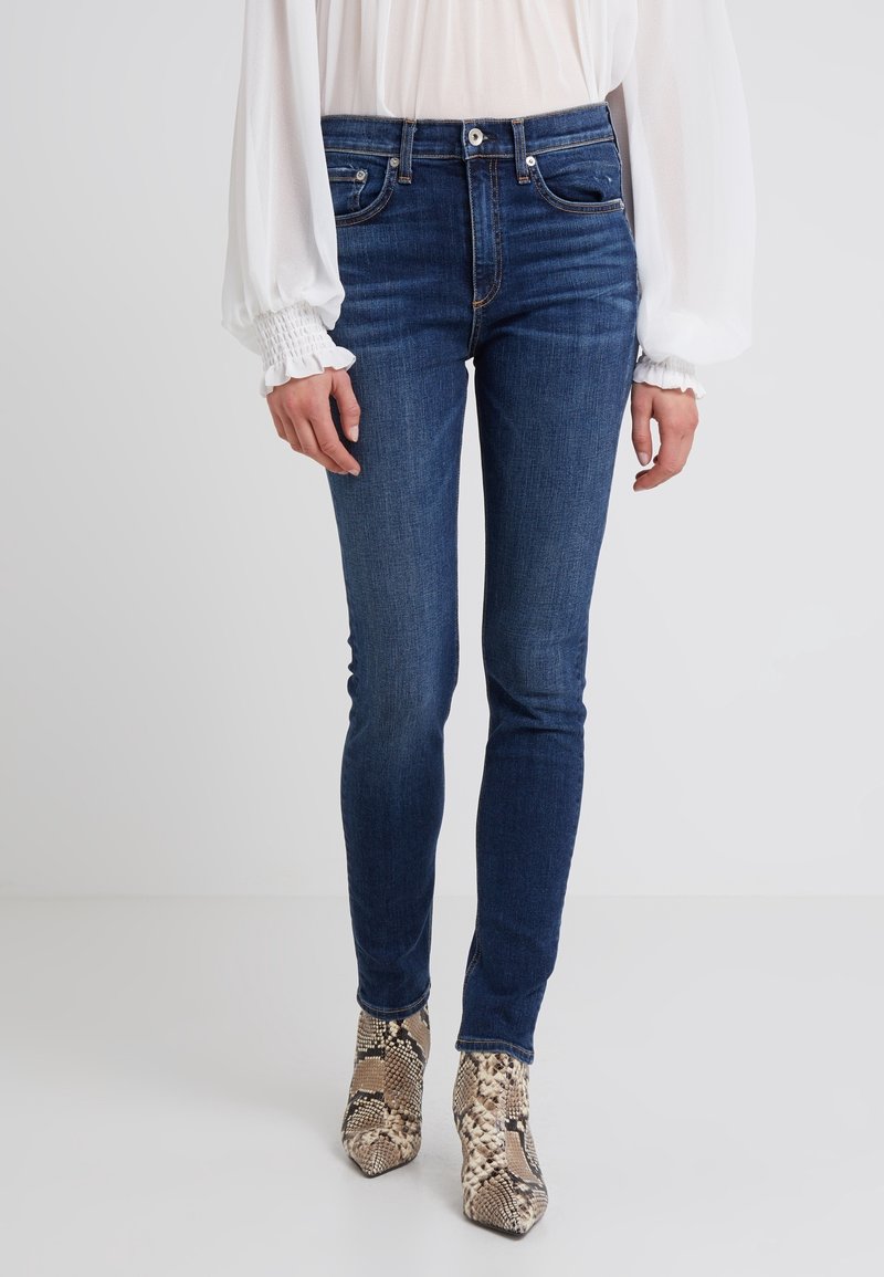 Vaqueros ajustados de mezclilla en color azul, con una cintura de altura media, diseño de cinco bolsillos y un desgaste sutil. Combinados con botas de tacón alto con estampado de serpiente.