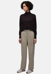 Schwarzer Rollkragenpullover, lockere Passform, beige strukturierte Hosen mit weitem Bein und Knopfverschluss sowie graue Sneaker mit dezenten gelben Akzenten.