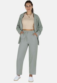 Leinenoutfit mit einem hellgrünen Langarmhemd, beigem Crop-Top und passenden Jogginghosen mit Kordelzug, ergänzt durch weiße Slippers.