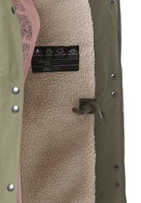 Groene geïsoleerde jas met een crèmekleurige nepbont voering, voorzien van een roze stoflaag en een etiket met onderhoudsinstructies met waterbestendige iconen.