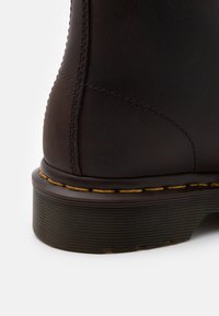 Gros plan du talon d'une botte en cuir marron foncé avec une semelle épaisse rainurée et une couture jaune le long de la bordure.
