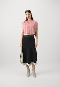 Rosa kort topp med høy hals, kombinert med et svart svajende skjørt med hvit kant. Tilbehør inkluderer en liten veske og beige ankelstøvler.