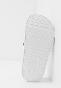 Suola di sneaker bianca con un motivo a spina di pesce texturizzato. Bordi lisci e una leggera curvatura. Design minimalista, senza branding visibile.