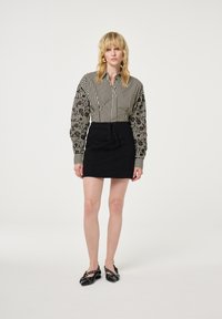 Zwarte rok met vetersluiting aan de voorkant, gecombineerd met een gestreepte blouse met gestippelde pofmouwen. Schoeisel is zwart met versieringen.