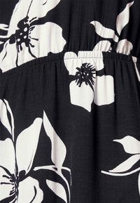 Schwarzer Stoff mit weißem Blumenmuster, das große Blüten und filigrane Details zeigt. Geraffter elastischer Taillenbund sorgt für Struktur.