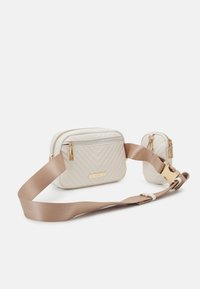 Krémová prošívaná kabelka přes rameno se zlatým kováním, hnědým popruhem a další malou kapsou. Má geometrický vzor a zapínání na zip.