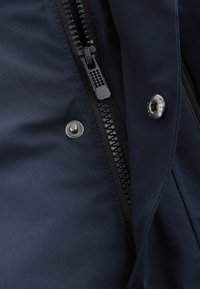 Tessuto blu navy dalla trama liscia con cerniera nera, chiusura a pressione e una delicata lucentezza. La cerniera è dotata di un tirante con texture.