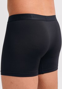 Schwarze, eng anliegende Boxershorts aus glattem, elastischem Stoff. Mit einem weichen Logo-Bund und einem Design in Mittelschenkel-Länge ohne sichtbare Nähte.