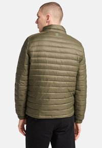 Olivgrön puffjacka med horisontellt quiltad struktur, hög krage och logodetalj på baksidan. Lättvikts- och åtsittande design.