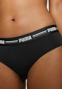 Schwarze Baumwollslips mit einem breiten elastischen Bund, der mit dem weißen "PUMA"-Logo und Streifen versehen ist. Glatte Textur, mittelhoher Schnitt und klassisches Design.